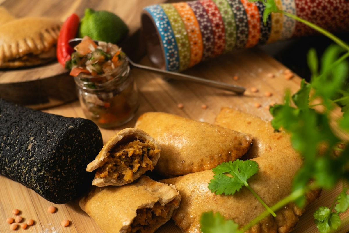 Hand-made empanadas on a wooden board with fresh coriander and salsa