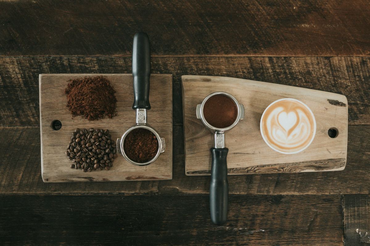 Coffee beans, ground espresso and a latte on wooden boards